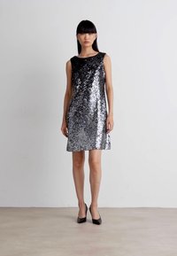 Abito argento con paillettes, design senza maniche, scollatura rotonda, forma a A e texture scintillante, abbinato a tacchi neri.