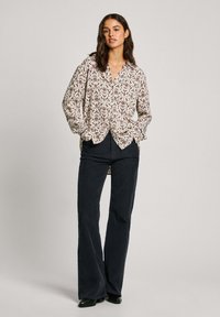 Camicia a fantasia floreale color crema con dettagli blu, rosa e verde, con colletto e chiusura a bottoni. Abbinata a pantaloni svasati blu scuro.