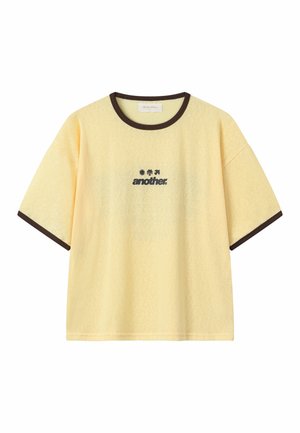 T-shirt jaune à manches courtes avec bordure marron foncé au niveau du col et des manches, avec le texte noir "another" et trois petites icônes au-dessus du centre de la poitrine.