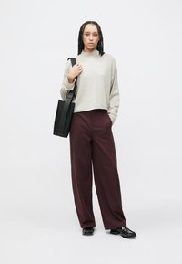 Bluza cu mânecă lungă de culoare gri deschis, pantaloni largi burduf maro închis, geantă tote din piele neagră cu bretele și pantofi negri lucioși. Fundal simplu.