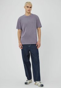 T-shirt lavande à manches courtes avec un col rond, associé à un jean en denim foncé ample avec des coutures contrastées et une silhouette décontractée.