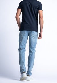 Vaqueros azul claro de corte ajustado, con bolsillos traseros y textura descolorida, combinados con una camiseta oscura y zapatillas blancas.