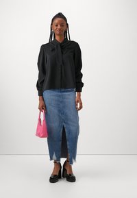 Svart langermet bluse med sløyfedetalj, kombinert med en blå denimskjørt med frontspalte, rosa håndveske, og svarte plattformhæler.