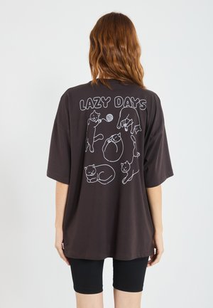 Dark brown oversized t-shirt featuring white line-drawn cats and the text "LAZY DAYS" on the back. Soft cotton material.