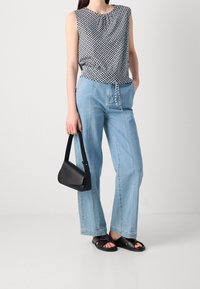 Top bez rukávů s geometrickým vzorem, světle modré široké džíny, černá kabelka přes rameno a černé ploché sandály.