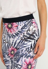 Blommig mönstrad kjol i vita, blå och rosa nyanser. Har ett svart elastiskt midjeband och en figurnära design med tropiska bladvinklar.