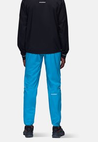 Svart jacka med långa ärmar, i kombination med ljusblå byxor. Båda har "Mammut"-logotypen. Byxorna har fickor med dragkedja och reflexdetaljer.