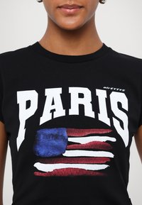 Black cotton t-shirt featuring "PARIS" in bold white letters, with a graphic of a stylized American flag in red, white, and blue.