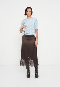 Pull en tricot bleu clair à manches courtes, associé à une jupe en satin marron avec une bordure en dentelle à l'ourlet, et des bottines noires pointues.
