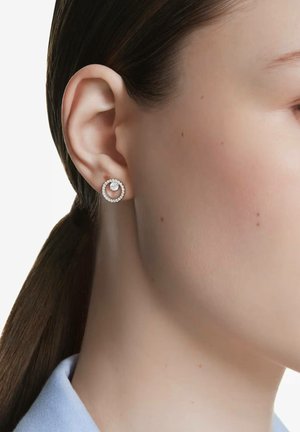 Boucles d'oreilles en argent avec un design circulaire orné de petites pierres précieuses claires, présentant une texture polie et une silhouette ouverte.