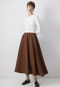Witte langemouw wraptop gecombineerd met een bruine enkellange rok van zachte stof, met een geplooide taille en een gladde textuur. Zwarte schoenen.