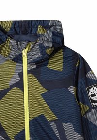 Bunda s kapucí v geometrickém vzoru v námořnické modři, žluté a šedé barvě. Má přední zip a texturovanou látku s logem.