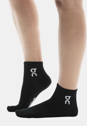 Chaussettes noires pour la cheville en tissu doux, avec un design côtelé et des accents de logo blanc sur le côté.