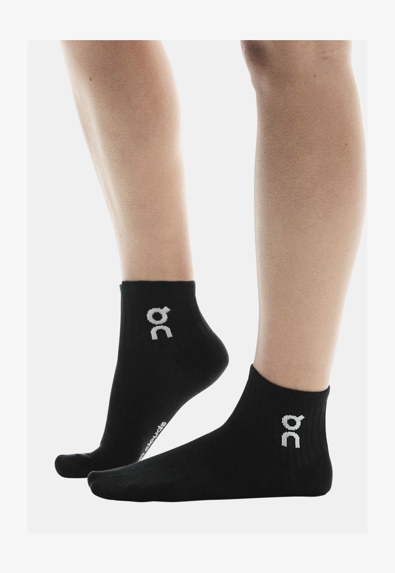 Calzini neri alla caviglia realizzati in tessuto morbido, con un design a costine e accenti di logo bianco sui lati.