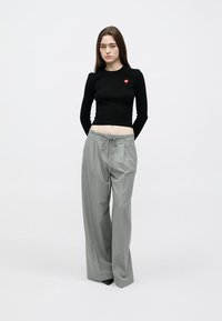 Top preto de manga comprida com um pequeno remendo em forma de coração vermelho, combinado com calças cinza claro, de cintura alta e perna larga, com cordão na cintura.