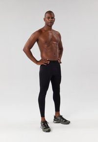 Juodos, prigludusios legging'os su lygiu paviršiumi, elastinga juosmens juosta ir be matomų raštų. Dėvimi su pilkiais sportiniais batais.