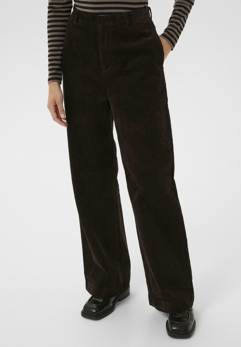 Bruine corduroy wijde pijpenbroeken met verticale ribbels. Heeft een hoge taille en zijzakken, gepaard met zwarte schoenen.