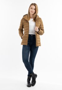Brun oppustet jakke med hætte, udstyret med lynlås og sidelommer, parret med mørke jeans og sorte ankelstøvler.