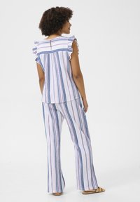 Set a due pezzi a righe composto da una maglietta a maniche corte con volant e schiena a oblò, abbinata a pantaloni a gamba larga, realizzato in un leggero tessuto a righe blu e rosa.