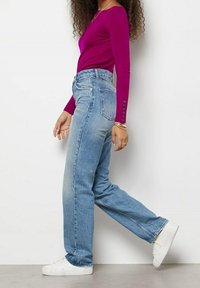 Dopasowana bluzka z długim rękawem w intensywnym magencie, w połączeniu z wysokim stanem jasnoniebieskich dżinsów i białymi sneakersami, prezentując swobodny styl.