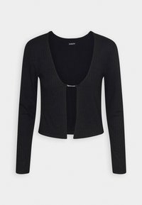 Musta ribatettu pitkähihaisten cropped-neule, jossa on syvä pyöreä kaula-aukko, ja joka on kiinnitetty pieneen rhinestone-soljella rinnassa.