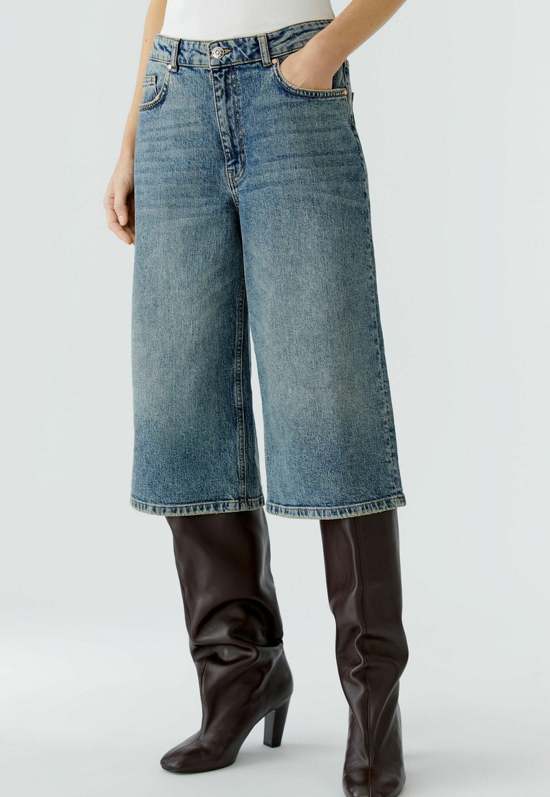 Denim culottes met een lichtblauwe wassing, hoge taille, twee zijzakken, met een relaxed fit en gestikte zoom, gecombineerd met bruine kniehoge laarzen.