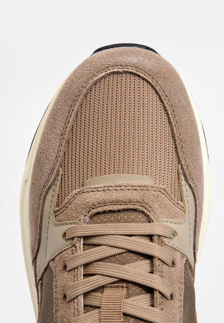 Baskets brunes avec un dessus texturé en mailles et en suède, des lacets proéminents et une semelle rembourrée avec un accent blanc.