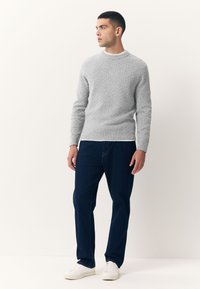 Maglione grigio chiaro lavorato a maglia con motivo strutturato, scollo rotondo e polsini a coste, abbinato a jeans blu scuro e sneakers bianche.