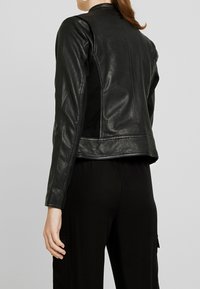 Svart läderjacka med slät textur, figurnära design och hög krage. Har sidopaneler och sömdetaljer.