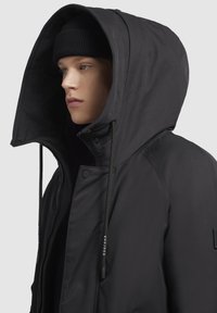 Czarna kurtka z kapturem o gładkiej powierzchni, z teksturowanym wewnętrznym podszewką, sznurkami ściągającymi i zatrzaskami z przodu.
