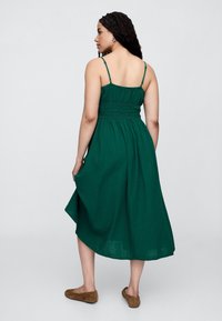 Zelené šaty po kolená s nastaviteľnými tenkými ramienkami, pružným živôtikom a plynulou sukňou. Vyrobené z ľahkej látky s textúrovaným povrchom.