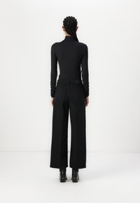 Crna majica s rol kragnom uparen s širokim crnim hlačama. Outfit se odlikuje glatkom teksturom i minimalističkim dizajnom, bez vidljivih uzoraka.