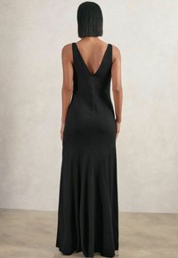 Černé maxi šaty bez rukávů s V-zadním výstřihem, přiléhavým živůtkem a rozšířeným lemem. Hladká textura s čistými liniemi a bez viditelných ozdob.