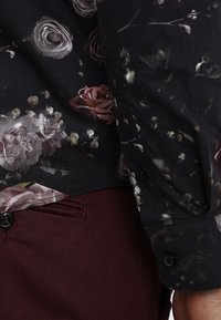 Musta paita, jossa on kukkakuosi, jossa on ruusuja vaaleanpunaisen ja harmaan sävyissä; yhdistettynä viininpunaisiin housuihin, joilla on sileä pinta ja nappidetail.