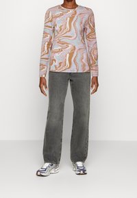 Langärmliges Shirt mit pinkem, braunem und blauem Marmor-Muster, kombiniert mit grauen geraden Jeans und mehrfarbigen Turnschuhen.