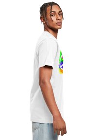 Hvid bomulds t-shirt med et farverigt abstrakt grafisk design med et fredssymbol, vist på en model fra siden.