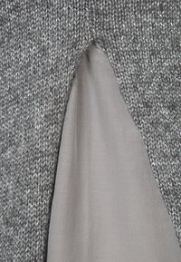 Tissu gris tricoté avec une découpe triangulaire révélant un matériau lisse de couleur gris clair en dessous.