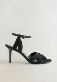Sort ruskinds højhælede sandal med tværstreg design, åben tå og ankelrem med cirkulær spænde detaljer.