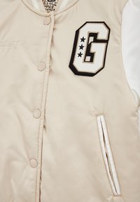 Šviesiai smėlinis bomber tipo švarkas su mustru G juodai baltos spalvos, mygtukais snap, ir baltais rankovėmis. Turi dvi šonines kišenes ir išsiuvinėtą tekstą.