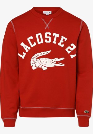 Sweat-shirt rouge avec texte blanc "LACOSTE 21" et grand logo crocodile blanc sur le devant, poignets côtelés, et emblème crocodile vert sur la manche.