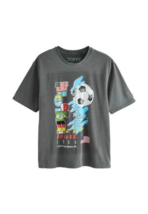 T-shirt gris avec texte coloré "WORLD CUP SOCCER 1994", un ballon de football, des illustrations du drapeau américain et une liste des villes hôtes sur le devant.
