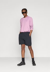 Ροζ ανοιχτόχρωμο μακρυμάνικο τοπ με υφή και μαύρο σορτς. Μαύρα γυαλιά ηλίου ολοκληρώνουν το αθλητικό λουκ, με σκούρα υποδήματα.