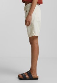 Shorts beige clair avec ourlets retroussés, poches avant et arrière, associés à des sandales à plateforme noires et en liège. Texture lisse, design décontracté.