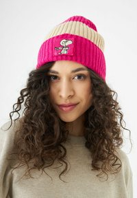 Bonnet tricoté rayé rose et crème avec un patch Snoopy. Texture côtelée, design ajusté et tissu doux.