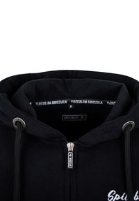 Schwarze Zip-Hoodie mit weichem Stoffgefühl, ausgestattet mit Kordelzügen, gesticktem Logo und einem Innenlabel mit "FLEISSIG AM ABKESSEN."
