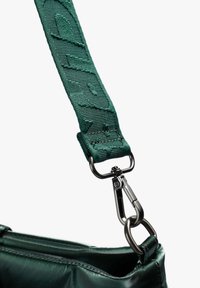 Bolsa de tela verde oscuro con una correa texturizada, que presenta un logotipo llamativo, clip de metal y una superficie lisa y brillante.