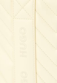 Καπιτονέ κρεμ δερμάτινη τσάντα με έντονο ανάγλυφο λογότυπο και αντίθετη ραφή. Υφή με διαγώνιο ζιγκ-ζαγκ μοτίβο.