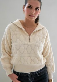 Crème, geweven quarter-zip pullover met diamantpatroon, geribbelde kraag en mouwen, gedragen met donkerblauwe jeans. Zacht, comfortabel stof.
