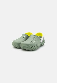 Green clogs made of rubber with a textured surface, featuring ventilation holes, bright yellow interior, and a white heel strap.
