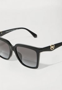 Ochelari de soare negri cu un cadru pătrat, lentile cu degradé și accent de logo aurit pe brațele laterale. Material plastic neted și design elegant.